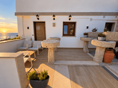 Terraza al atardecer de la cabaña Holibai en As Mariñas, España, con mesas de piedra, asientos al aire libre y vistas al mar