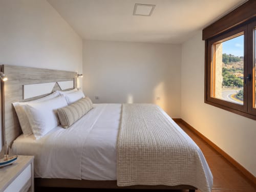 Dormitorio moderno en cabaña Holibai en As Mariñas con vistas al mar, ropa de cama blanca, cabecero de madera y vistas al paisaje de colinas