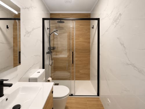 Baño moderno en la cabaña Holibai con paredes de mármol, detalles en madera, mampara de ducha con marco negro, lavabo y inodoro blancos