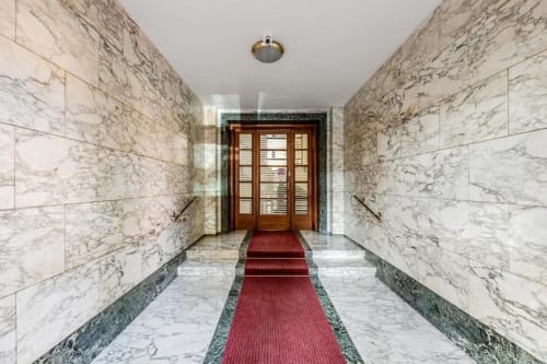 Elegante corridoio rivestito in marmo presso l'Amor Rome Apartment con tappeto rosso e porta d'ingresso in legno