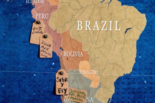 Mappa del Sudamerica con etichette di paesi scritte a mano e targhette in legno che segnano destinazioni come Perù, Bolivia e Paraguay
