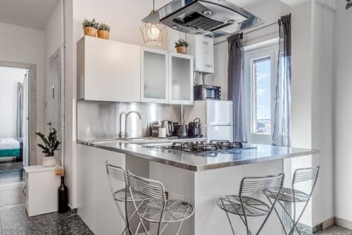 Moderna cucina bianca con piano in acciaio inox, fornello a gas e bancone bar nell'Amor Rome Apartment a Roma