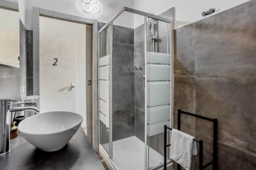 Bagno moderno nell'Apartment Amor Roma con lavabo rotondo, cabina doccia in vetro e piastrelle scure alle pareti