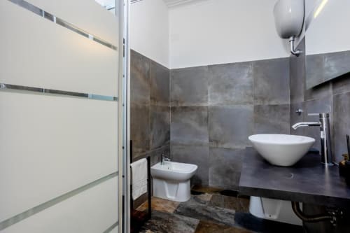 Bagno moderno dell'Amor Rome Apartment con rivestimenti in piastrelle scure, lavabo bianco, bidet e soffione pioggia a Roma, Italia