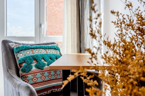 Accogliente stanza romana con poltrona, coperta turchese, fiori secchi e vista dalla finestra su edifici in mattoni