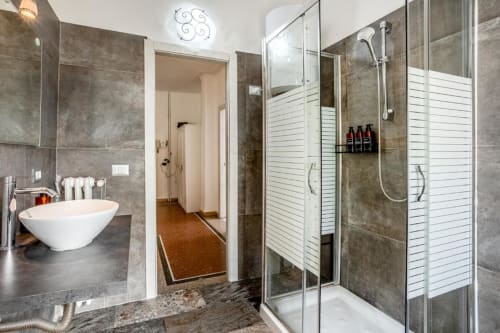 Bagno moderno dell'Amor Rome Apartment con piastrelle grigie, lavabo bianco in ceramica, cabina doccia in vetro e scaldasalviette elettrico