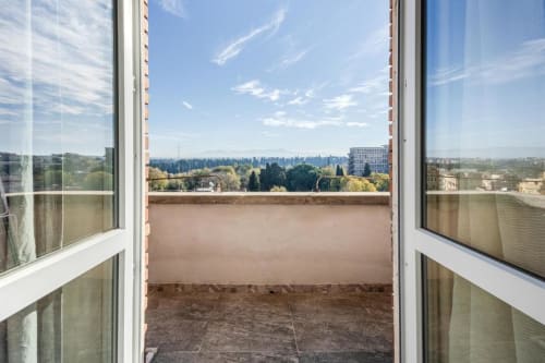Porte balconate aperte che rivelano lo skyline di Roma con paesaggio verde, alberi e panorama urbano dall'Aparthotel Amor Rome