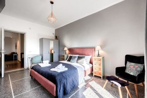 Camera da letto moderna dell'Amor Rome Apartment con letto rosa, biancheria blu navy, comodino in legno e poltrona nera