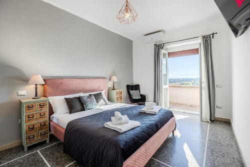 Camera luminosa dell'Amor Rome Apartment con testata rosa, letto trapuntato blu, comodino in legno e vista della terrazza su Roma