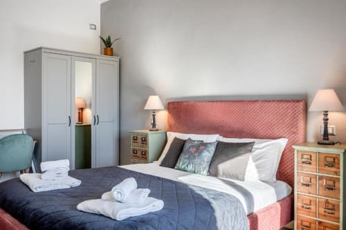Camera da letto dell'Amor Rome Apartment con testiera color corallo, biancheria bianca, comodini in legno e arredamento elegante
