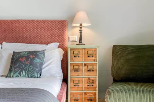 Camera da letto dell'Amor Rome Apartment con testata corallo, cuscino floreale, comodino in legno, lampada da tavolo e sedia verde