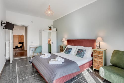 Spaziosa camera da letto all'Amor Rome Apartment con testata rossa, lampade gemelle, poltrona verde e moderna lampada a sospensione a Roma, Italia