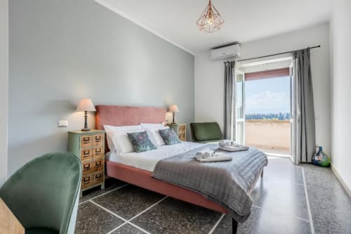 Camera da letto moderna all'Amor Rome Apartment con letto rosa, poltrona verde, comodini in legno e vista balcone su spiaggia e città