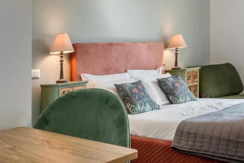 Camera da letto dell'Amor Rome Apartment con testiera rosa, comodini verdi, lampade da tavolo, cuscini decorati e scrivania in legno