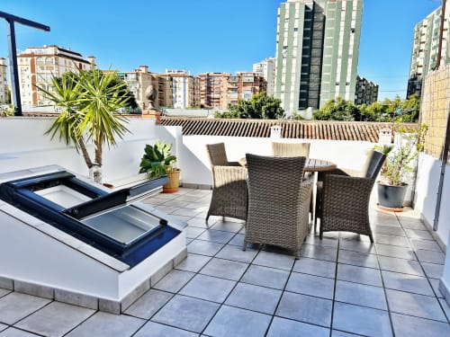 Terraza en la azotea de Fuengirola con muebles de mimbre, claraboya, plantas en macetas y vistas a edificios bajo cielo azul