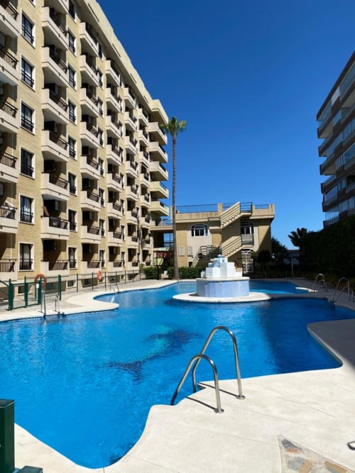 Piscina azul con escalera y fuente central en el hotel Grupo Inmohouse de Fuengirola, España, rodeada de tonos beige