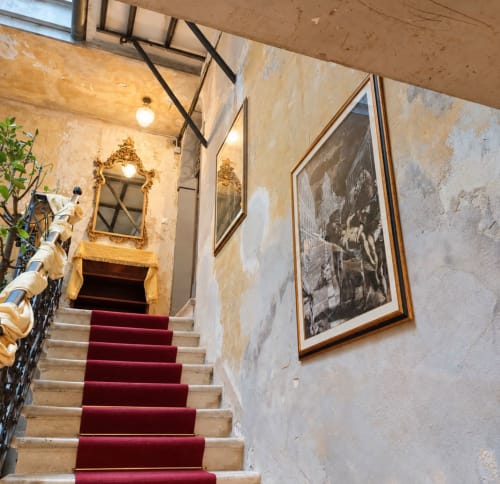 Grande scalone con tappeto rosso a Palazzo Titti Venezia, specchio ornato e quadri incorniciati su muri invecchiati