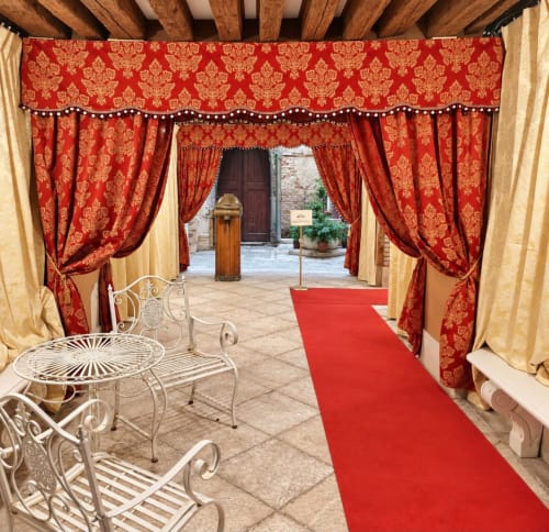 Elegante ingresso del cortile di Palazzo Titti Venezia con sontuosi tendaggi rossi damascati, tappeto rosso, mobili in ferro battuto bianco