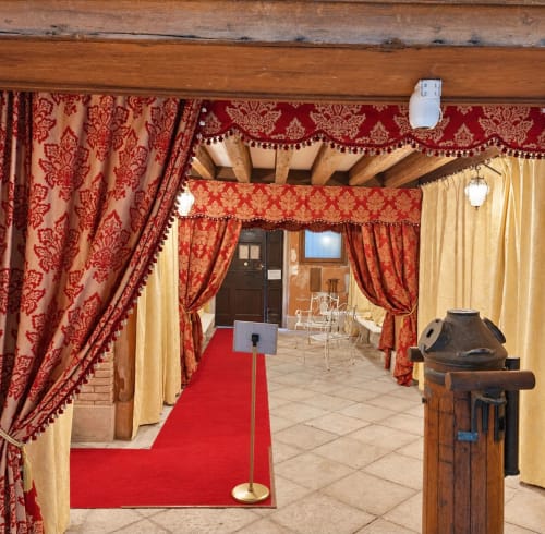 Atrio del Palazzo Titti a Venezia con tendaggi in damasco rosso, drappeggi dorati, travi in legno e tappeto rosso verso le porte d'ingresso