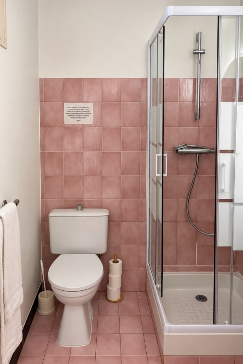 Salle de bain moderne aux murs carrelés rose, toilettes blanches et douche vitrée à l'Hôtel Thalassa de Cargèse