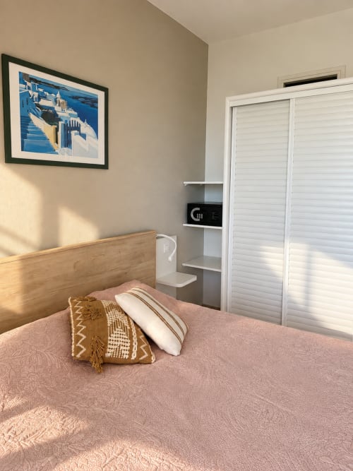 Chambre lumineuse à l'Hôtel Thalassa à Cargèse avec literie rose, tête de lit en bois, étagères intégrées et portes de placard blanches