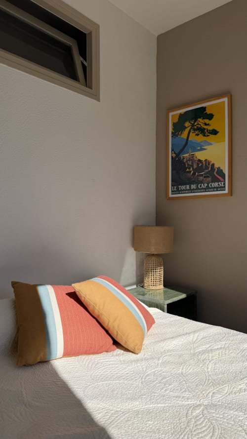 Chambre à l'Hôtel Thalassa à Cargèse avec coussins colorés, lampe en rotin et affiche vintage de voyage en Corse