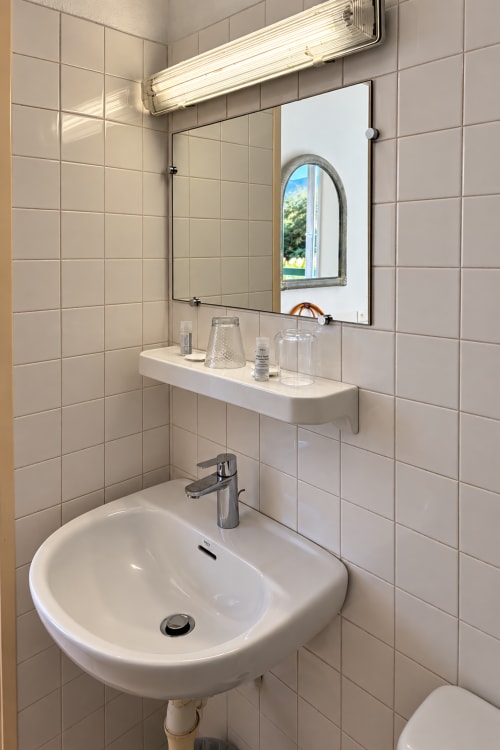Lavabo moderne avec miroir et tablette de rangement à l'Hôtel Thalassa, Cargèse, aux murs en carrelage blanc et éclairage ambiant