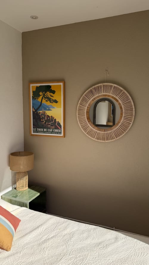 Coin chambre à l'Hôtel Thalassa à Cargèse avec affiche vintage de Corse, miroir tressé et lampe en rotin sur la table de nuit