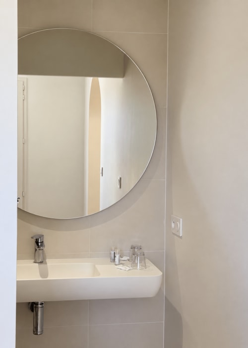 Salle de bain moderne de l'Hôtel Thalassa Cargèse avec miroir rond et lavabo blanc