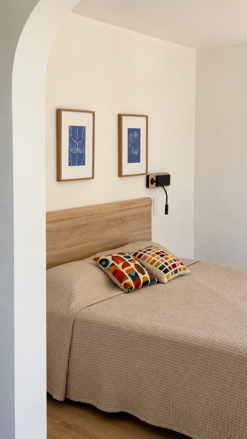 Chambre supérieure de l'Hôtel Thalassa à Cargèse avec lit en bois, œuvre d'art encadrée bleue et coussins colorés