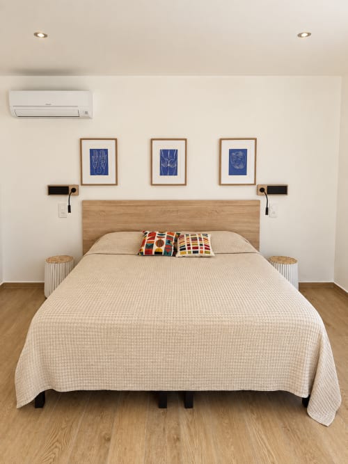 Chambre lumineuse à l'Hôtel Thalassa Cargèse avec lit en bois, literie crème, œuvres d'art bleues et équipements modernes