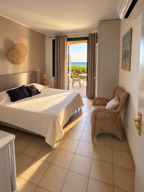 Chambre côtière lumineuse à l'Hôtel Thalassa avec vue mer depuis la terrasse, fauteuil en rotin et mobilier crème
