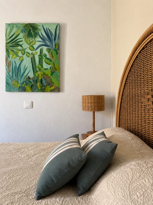 Chambre de l'Hôtel Thalassa Cargèse avec œuvres d'art tropicales, tête de lit tressée, oreillers rayés et lampe en rotin