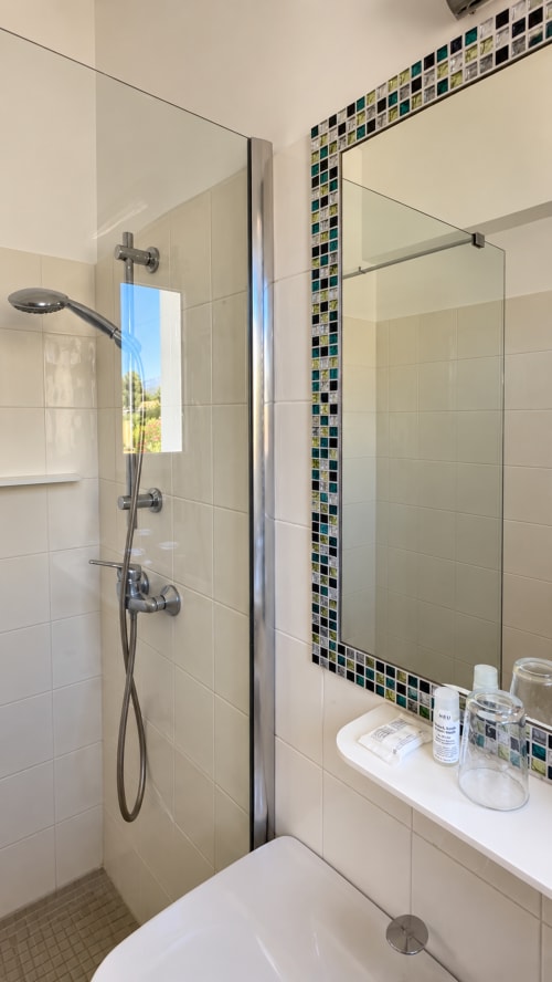 Salle de bain moderne à l'Hôtel Thalassa à Cargèse avec douche en verre, frise en carrelage mosaïque et accessoires de toilette sur le comptoir