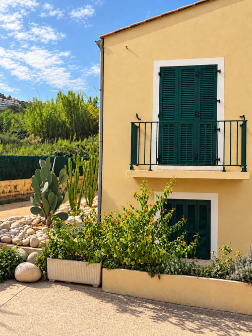 Chambre Hôtel Thalassa à Cargèse avec façade jaune, volets verts et jardin méditerranéen