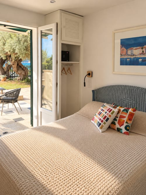 Chambre lumineuse à l'Hôtel Thalassa à Cargèse avec vue mer, tête de lit en rotin et portes-fenêtres sur terrasse