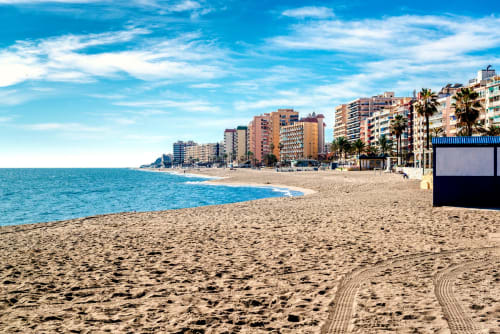 Playa de Fuengirola con arena blanca, mar turquesa, palmeras y edificios de apartamentos frente al mar bajo cielo azul
