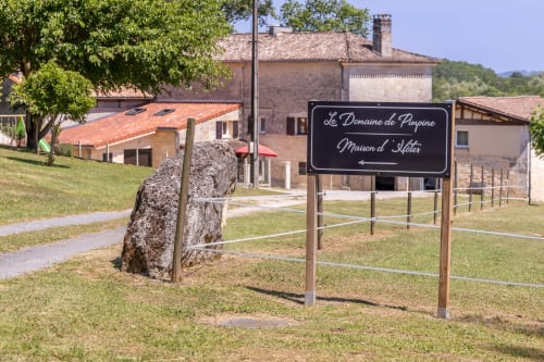 Panneau d'entrée du Domaine de Pimpine Maison d'Hôtes à Galgon, France, avec bâtiments historiques en pierre visibles en arrière-plan