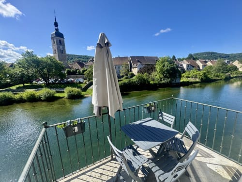 Balcon sur la rivière aux Tanneries, Ornans avec parasol, table et chaises surplombant la Loue et l'église