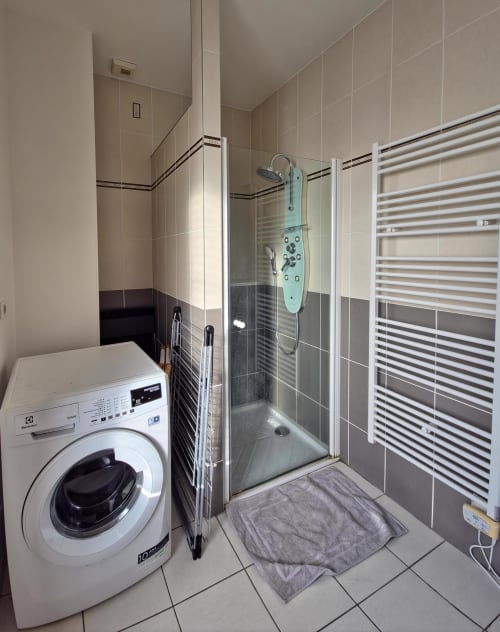 Salle de bain moderne dans l'appartement Les Tanneries à Ornans avec douche, lave-linge et radiateur sèche-serviettes