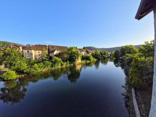 Vue riveraine d'Ornans avec bâtiments historiques reflétés dans une eau calme, localisation de l'hôtel Les Tanneries