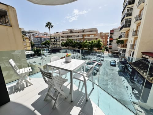 Moderna terraza en azotea con mobiliario de comedor blanco con vistas a la calle de Fuengirola y edificios mediterráneos