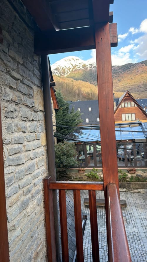 Puerta-ventana de madera abierta a vistas de montaña, bosques de pinos y edificios de piedra en Vielha, Andorra