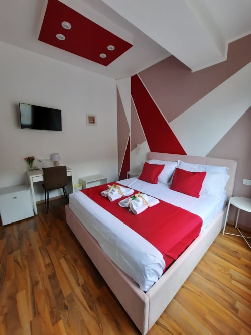 Camera moderna presso U Baruni b&b Messina con biancheria rossa e bianca, soffitto geometrico, TV, pavimenti in legno e vista sulla città