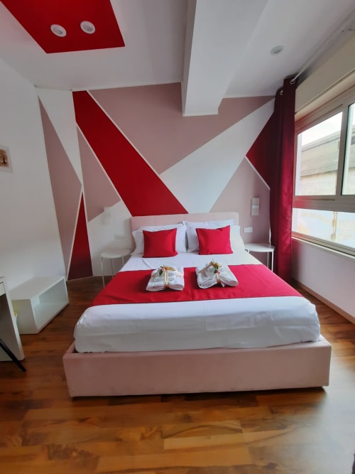 Camera moderna presso U Baruni b&b Messina con parete a design geometrico rosso e bianco, letto matrimoniale con biancheria rossa, pavimento in legno