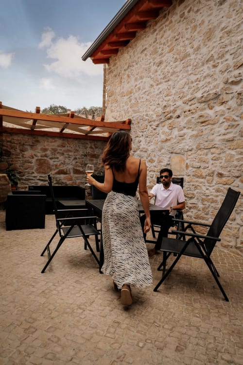 Mulher desfrutando de um copo de vinho na varanda externa do hotel Recantos D'Almerinda em Pombal, Portugal, com paredes de pedra