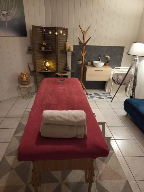 Salle de massage spa du gîte Chez Mariebel' à Ottonville avec lit de soin rouge, serviettes et accessoires en bois