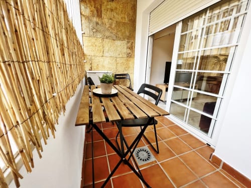Soleada terraza con mesa de madera, sillas negras y baldosas de terracota en apartamento de Fuengirola