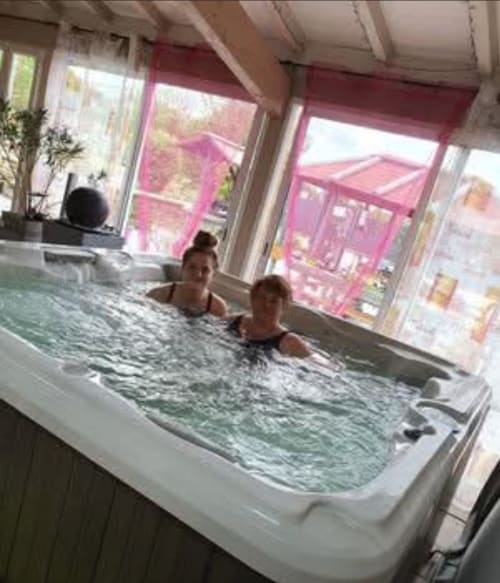 Two guests enjoying the heated indoor jacuzzi at Chez Mariebel' cottage in Ottonville, France, with garden views through