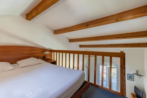Bright bedroom with wooden beams, queen bed, railing, and garden view doors at Domaine de la Bégude, Fayence